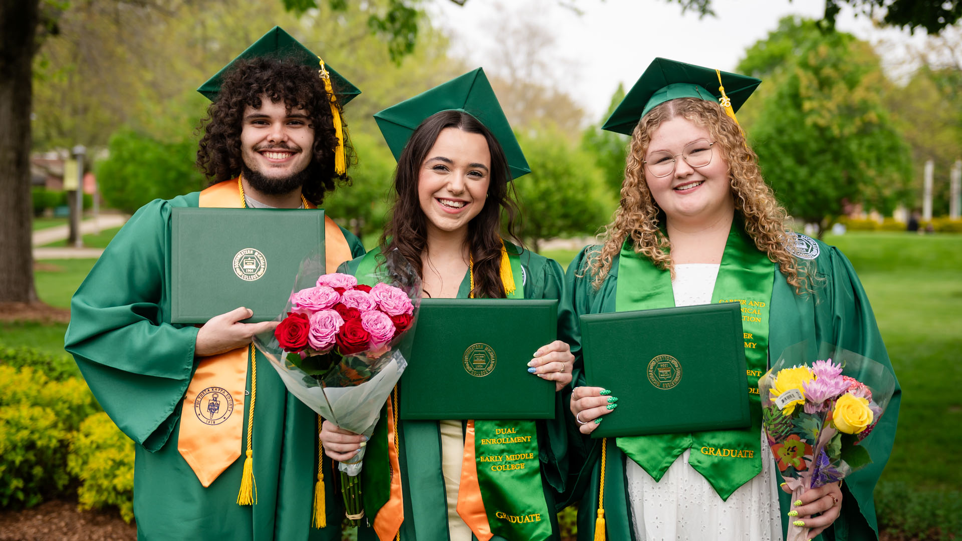 Three student posing for a photo in their commencement cap and gown