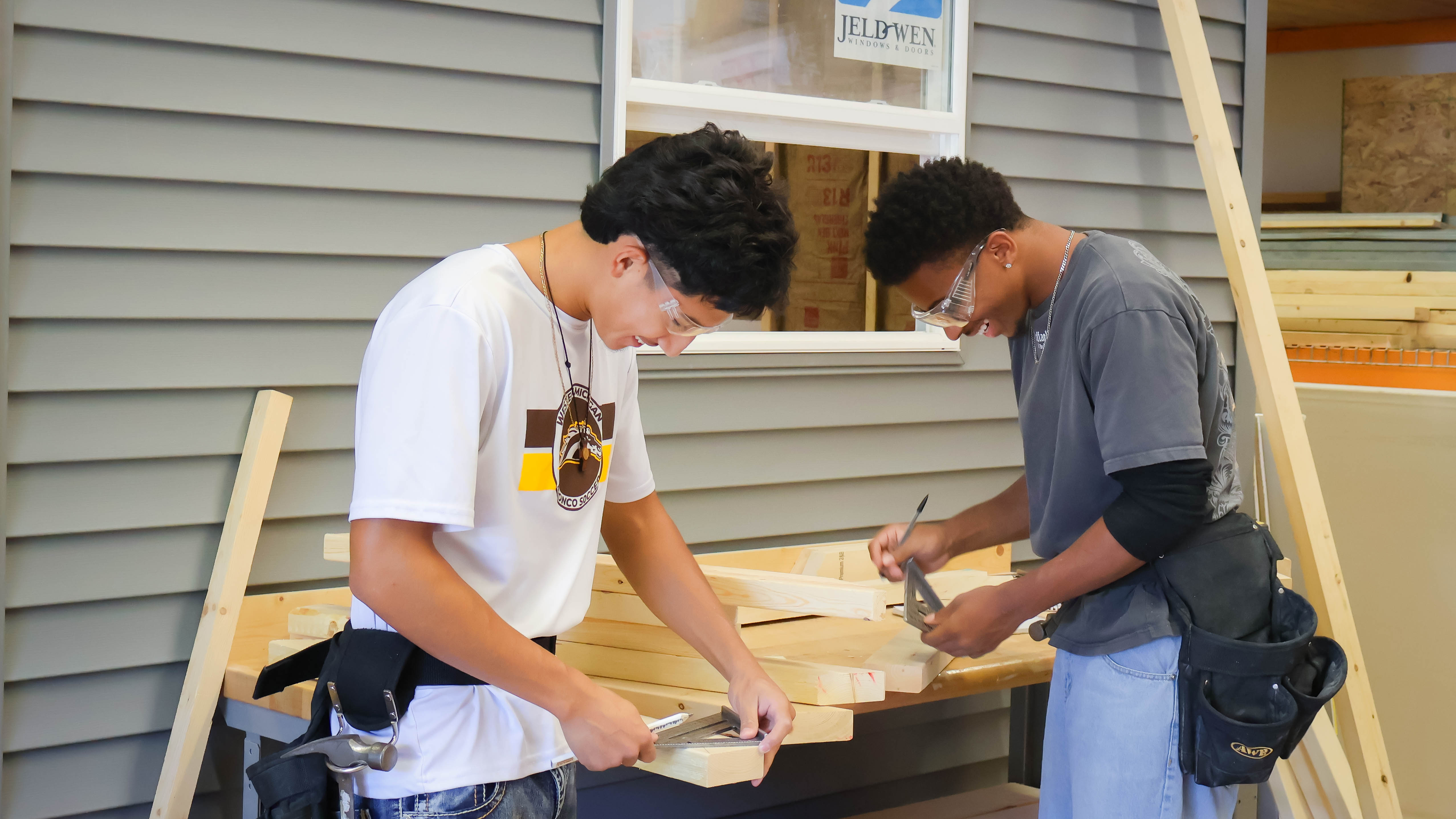 An image of two students in the construction program smiling and working together to cut wood.